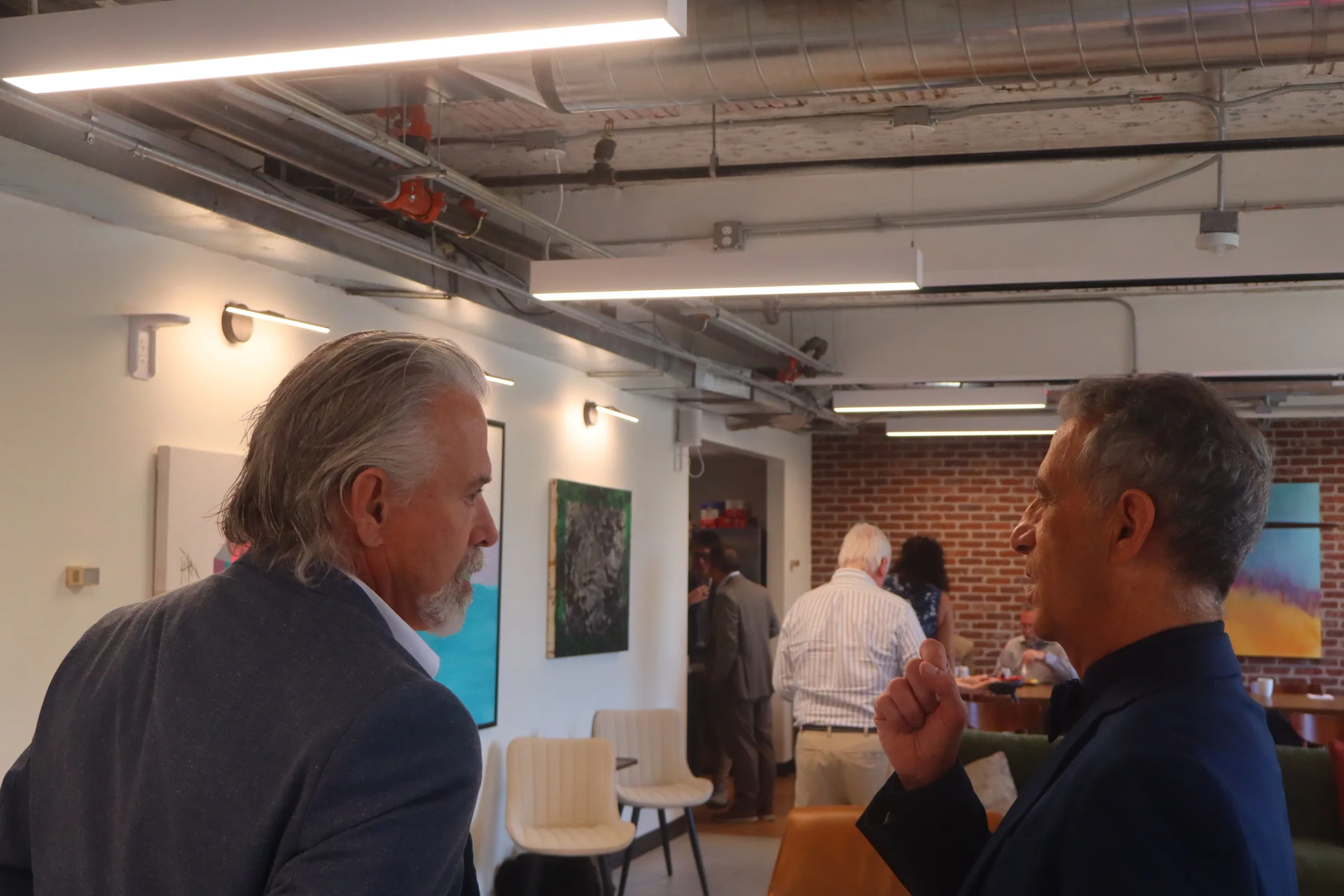 Two attendees in conversation at the reception, artwork and exposed brick behind them.